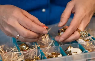 Unternehmerin Karin sortiert Schmuck in einer Box am Arbeitsplatz. 